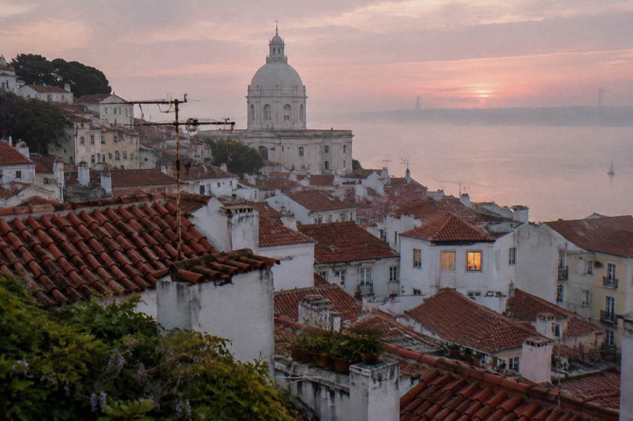 View over Lisbon rooftops towards the Tagus River with terracotta buildings and a church dome