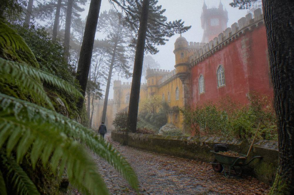 The red and yellow western facade of Pena Palace seen from a path in the surrounding park