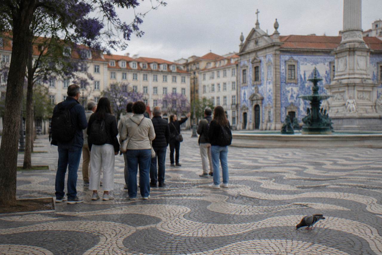 A small group of visitors gathered around a guide at a Lisbon square with tiled facades behind them